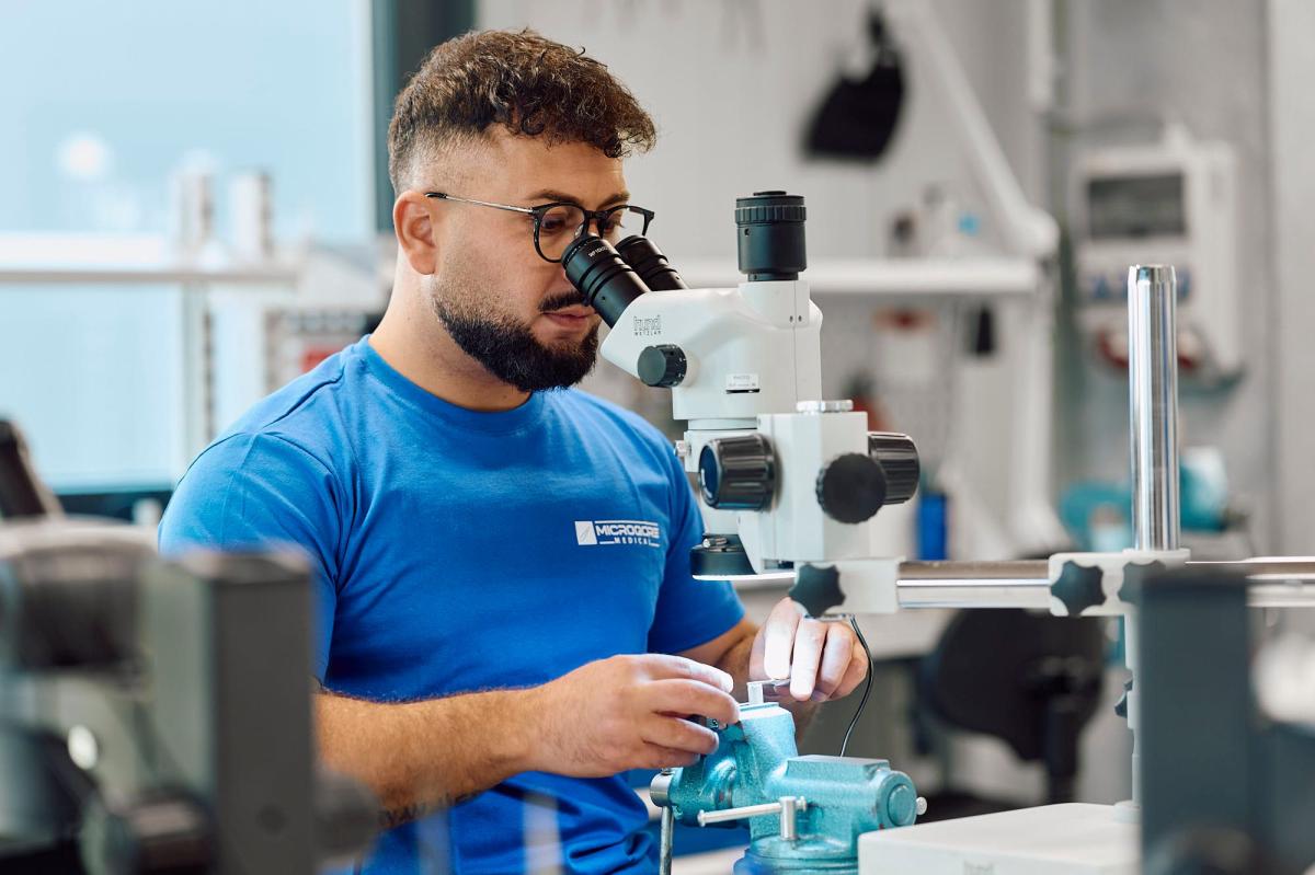 Mitarbeiter bei der Arbeit mit chirurgischen Präzisionsinstrumenten unter dem Mikroskop.