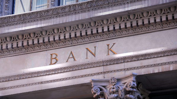Die Fassade einer Bank zeigt das Wort 'BANK' und thematisiert Tagesgeldkonto Risiken.