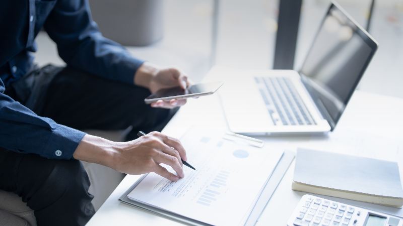 Person analysiert Finanzdaten und Smartphone am Arbeitstisch für Tagesgeldkonto.