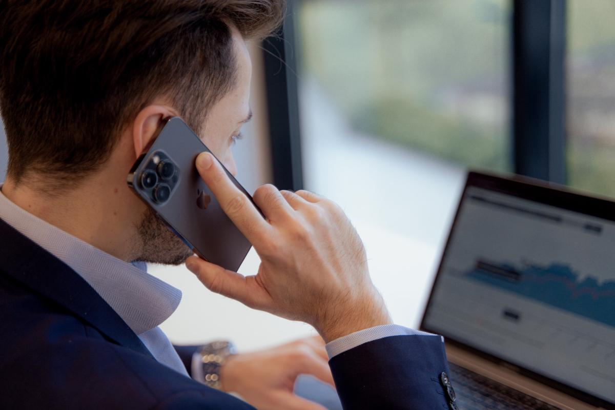 Mann telefoniert über Smartphone und arbeitet an Laptop während er über Immobilien als Kapitalanlage nachdenkt.