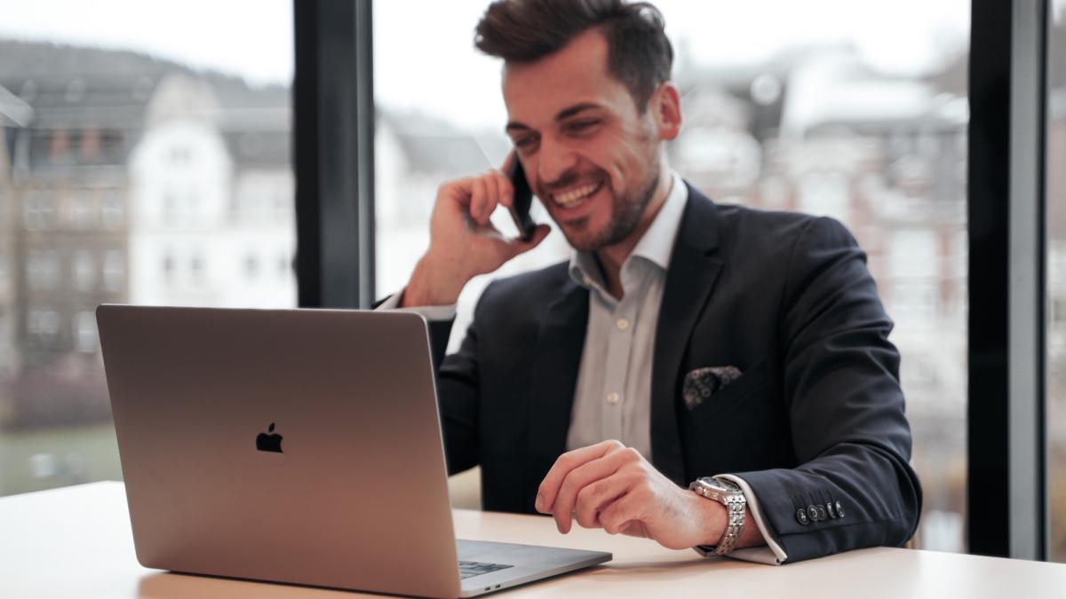 Mann am Laptop telefoniert über sein Wertpapierdepot bei der Hausbank.