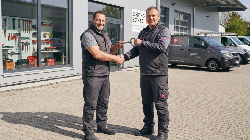 Zwei Männer bei der Schlüsselübergabe im Handwerk während des Unternehmensverkaufs.
