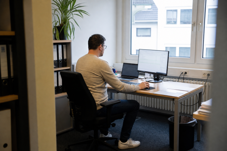 Ein Mitarbeiter sitzt an seinem Schreibtisch und arbeitet mit KI-Tools, was Erschöpfung verursachen kann.