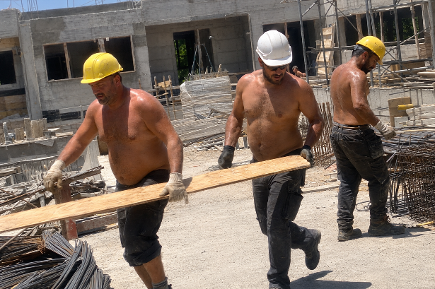 Bauarbeiter ohne Hemd tragen Holzplatten bei Hitze am Arbeitsplatz.