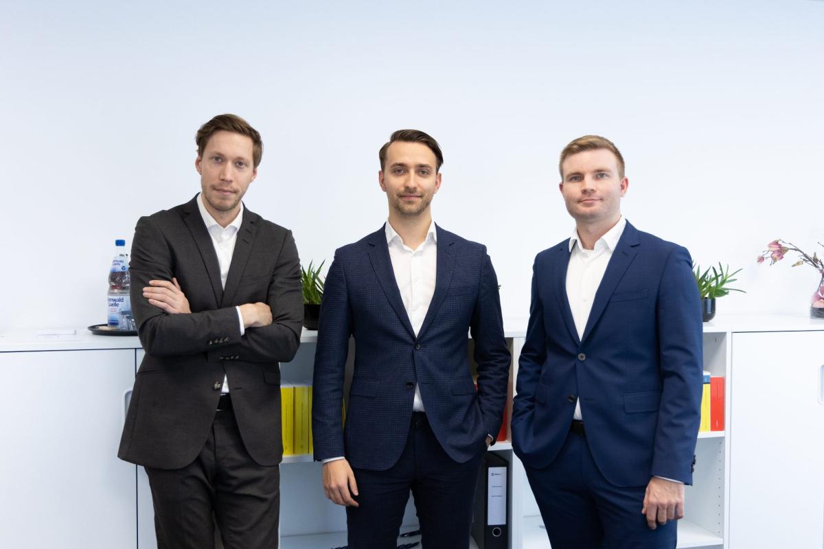 Drei Geschäftspartner in Anzügen stehen in einem modernen Büro für Mandantengewinnung der Steuerkanzlei.