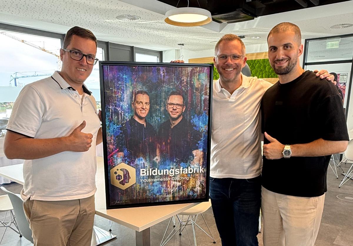 Drei Personen posieren mit einem Poster zur Bildungsfabrik, das KI als Mitarbeiter thematisiert.