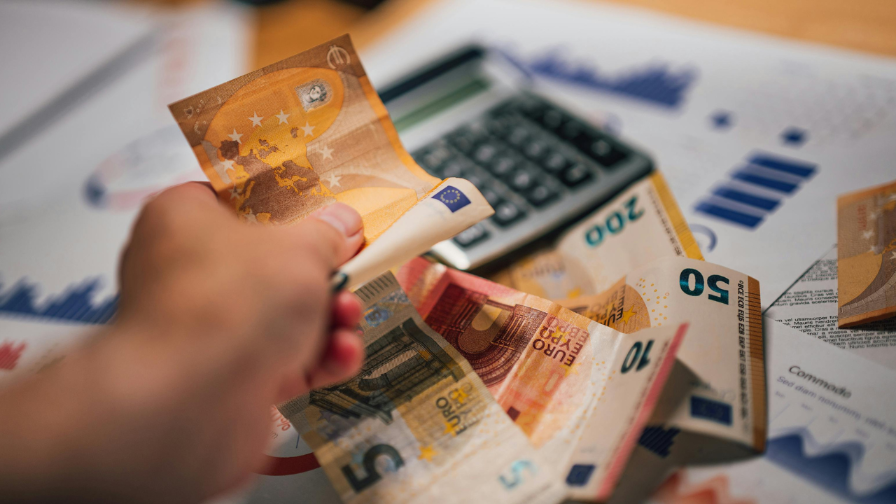 Ein Geldschein wird gehalten, umgeben von Euro-Scheinen und einem Taschenrechner im Kontext von BaFin Bußgeld TeamViewer.