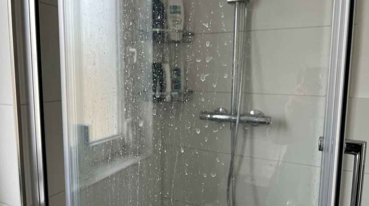 Nasses Duschglas zeigt Kalkreste, Duschglas reinigen hilft, Ablagerungen zu vermeiden.