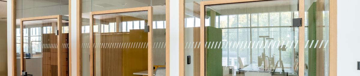 Moderne Bürotrennwand aus Glas mit Holzrahmen zur akustischen Raumteilung.