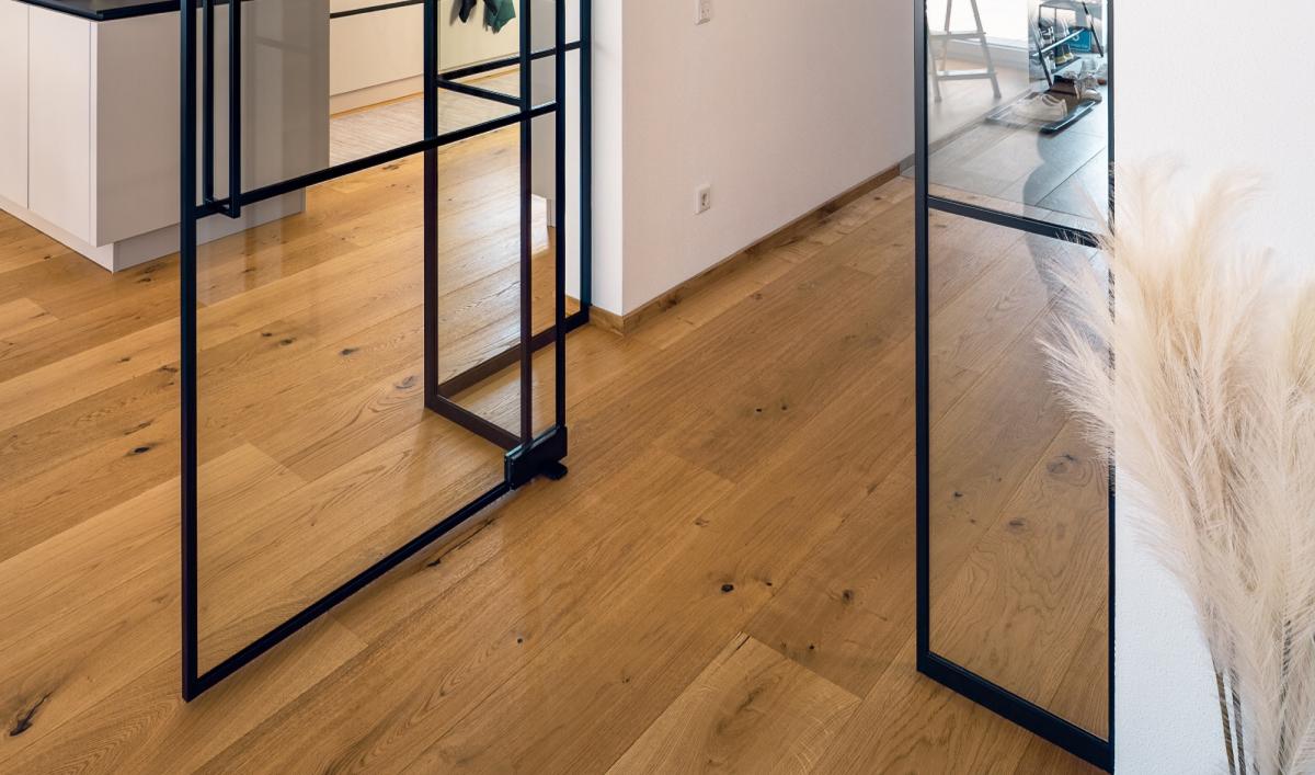Glastrennwand mit Tür und schwarzen Sprossen trennt einen Wohnbereich mit Holzboden.