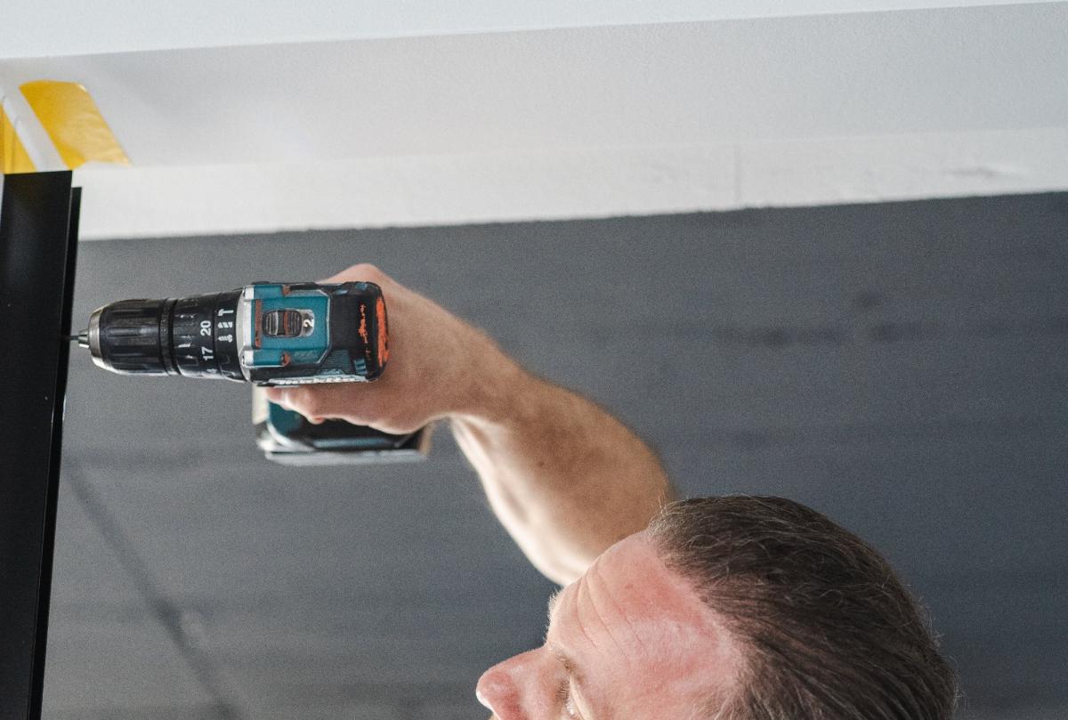 Ein Handwerker befestigt mit einem Akkuschrauber ein schwarzes Profil an der Decke für Glastrennwände im Autohaus.
