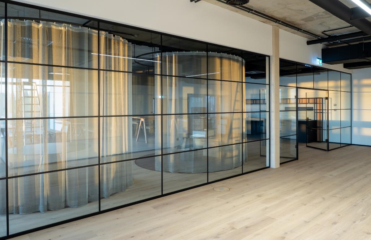 Moderne Raumtrennung aus Glas mit transparenten und festen Bereichen in einem Büro.