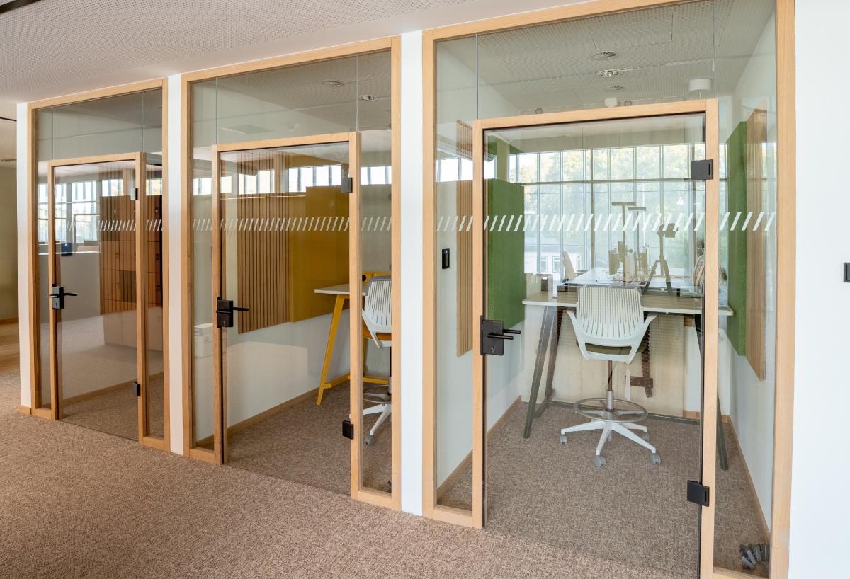 Akustik-Trennwand im Büro aus Glas mit mehreren Türen und eingerichteten Besprechungsräumen.