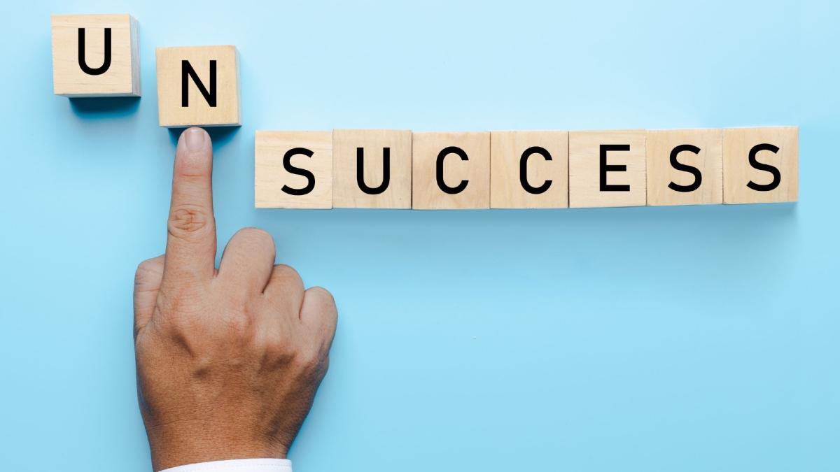 Eine Hand zeigt auf den Block mit den Buchstaben 'UN' vor dem Wort 'SUCCESS', symbolisiert inneren Erfolg.