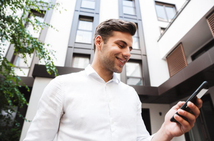 Mann in weißem Hemd schaut auf sein Smartphone, wichtig für Social Media für Immobilienmakler.