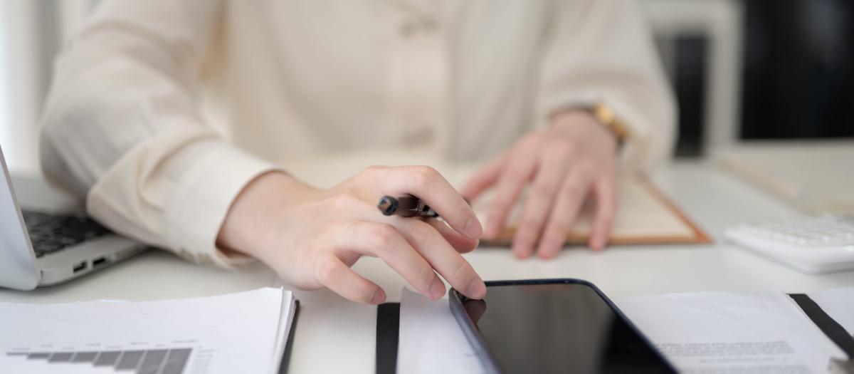 Hand eines Maklers beim Arbeiten mit Handynummern und Unterlagen zu Leads.