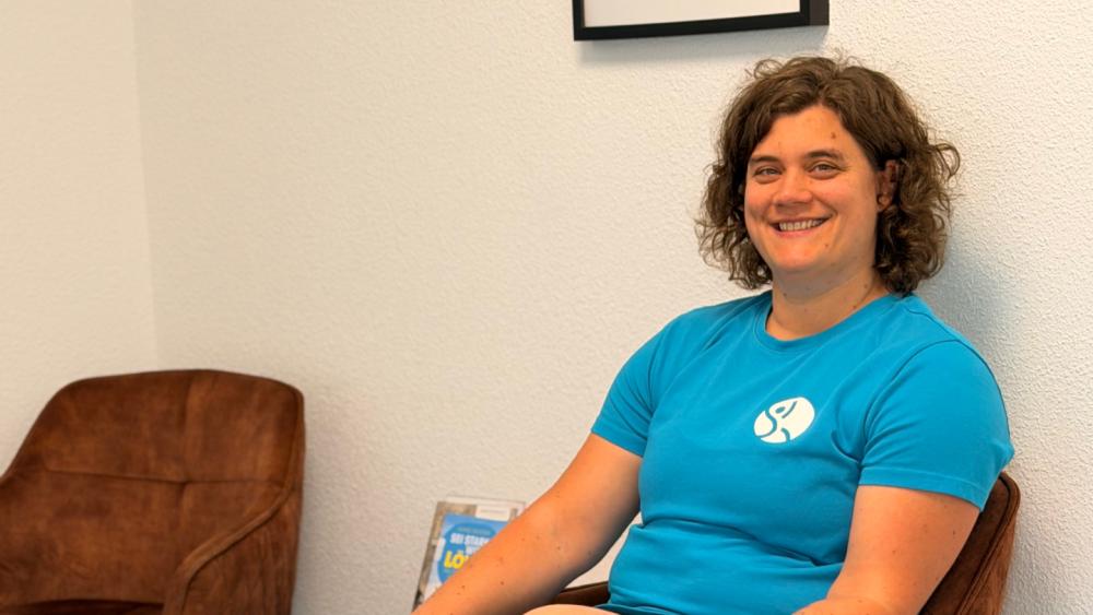 Eine Frau in blauer Kleidung sitzt entspannt in einem Stuhl und demonstriert richtiges Sitzen.