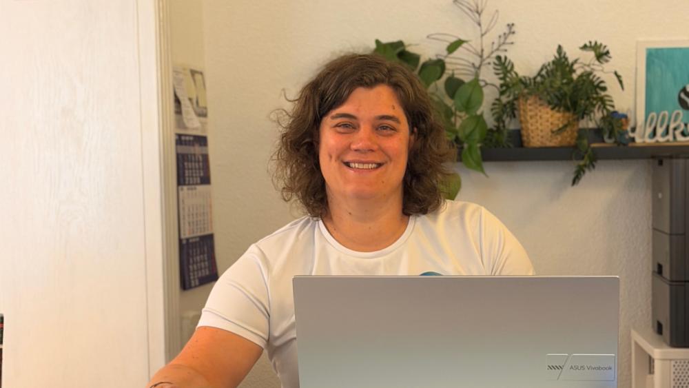 Eine lachende Person am Computer erklärt den 12-Wochen-Plan gegen Schmerzen.