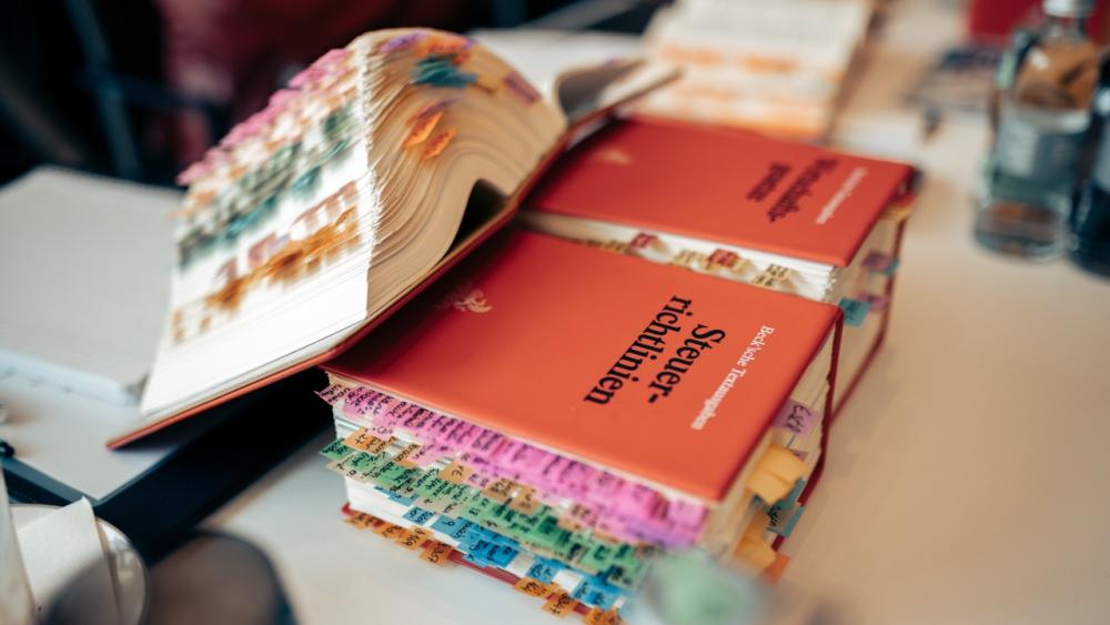 Auf einem Tisch liegen Lehrbücher zur Steuerberaterprüfung mit bunten Tabs.