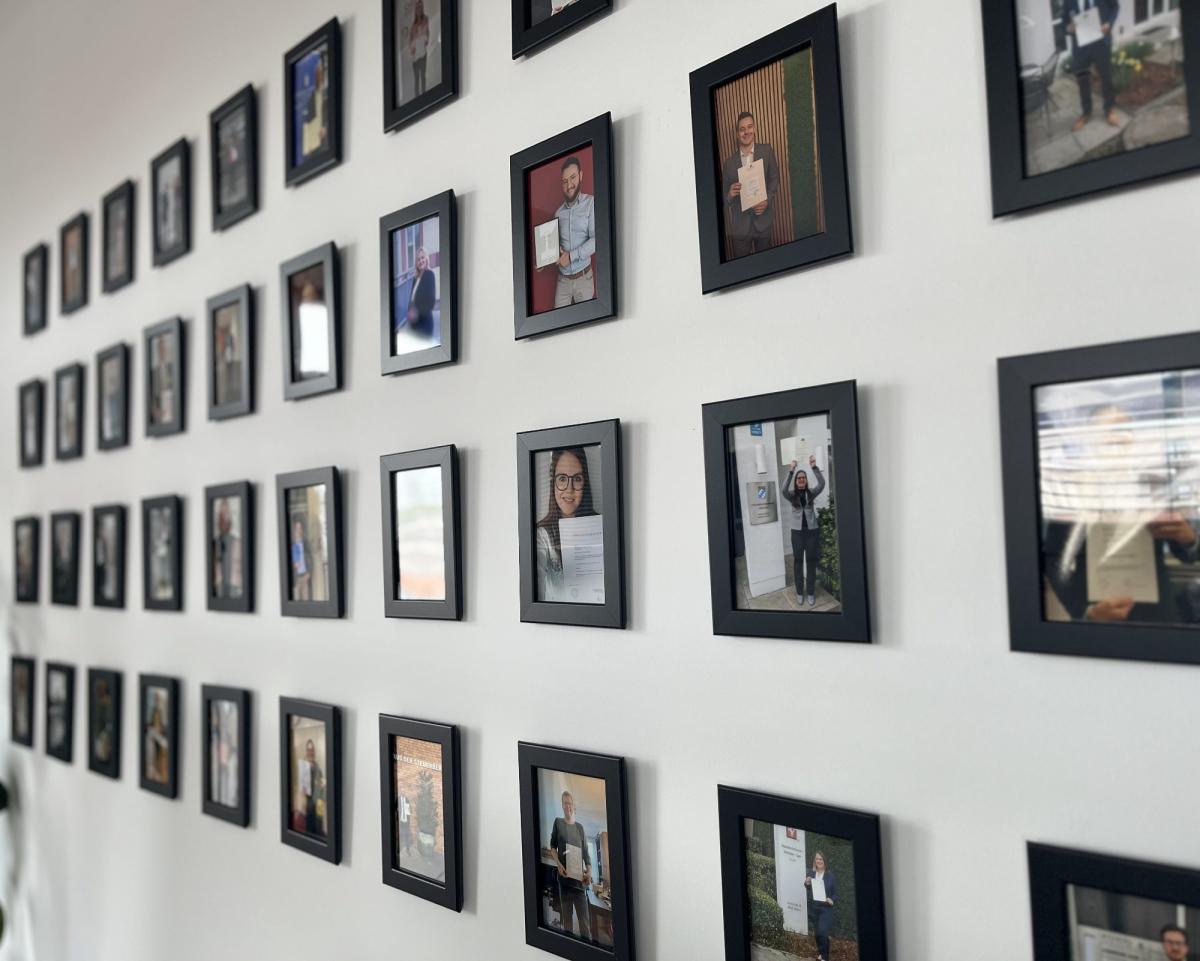Wand mit Rahmen von Fotos, die verschiedene Zertifizierungen zeigen, betont die ISO- und AZAV-Zertifizierung.