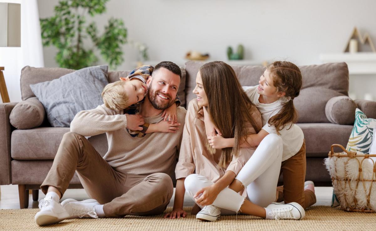Eine glückliche Familie sitzt im Wohnzimmer und lacht miteinander.