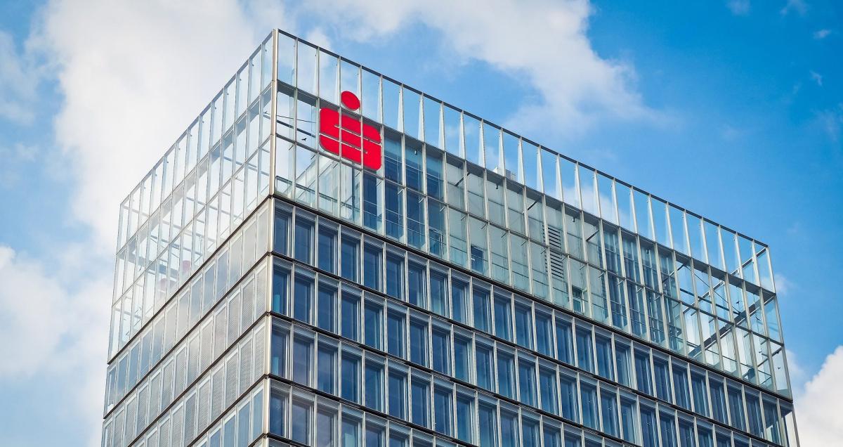 Modernes Gebäude mit Glasfassade und rotem Logo, symbolisiert Firmenkonto und Liquidität.