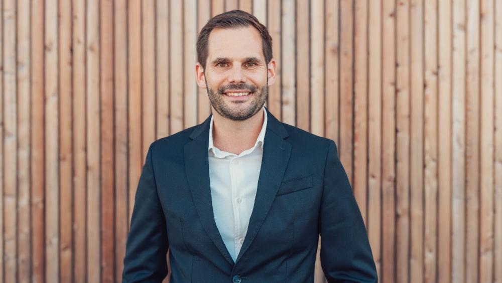 Benedikt Hausler im dunklen Anzug vor einer Holzwand – Gold-Silber SWITCH als Thema seines Angebots.