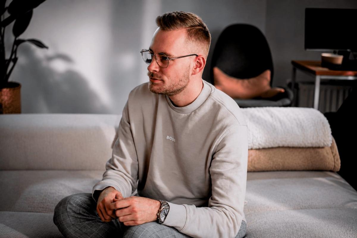 Ein junger Mann sitzt nachdenklich auf einem Sofa, was die Idee authentische DJs verkörpert.