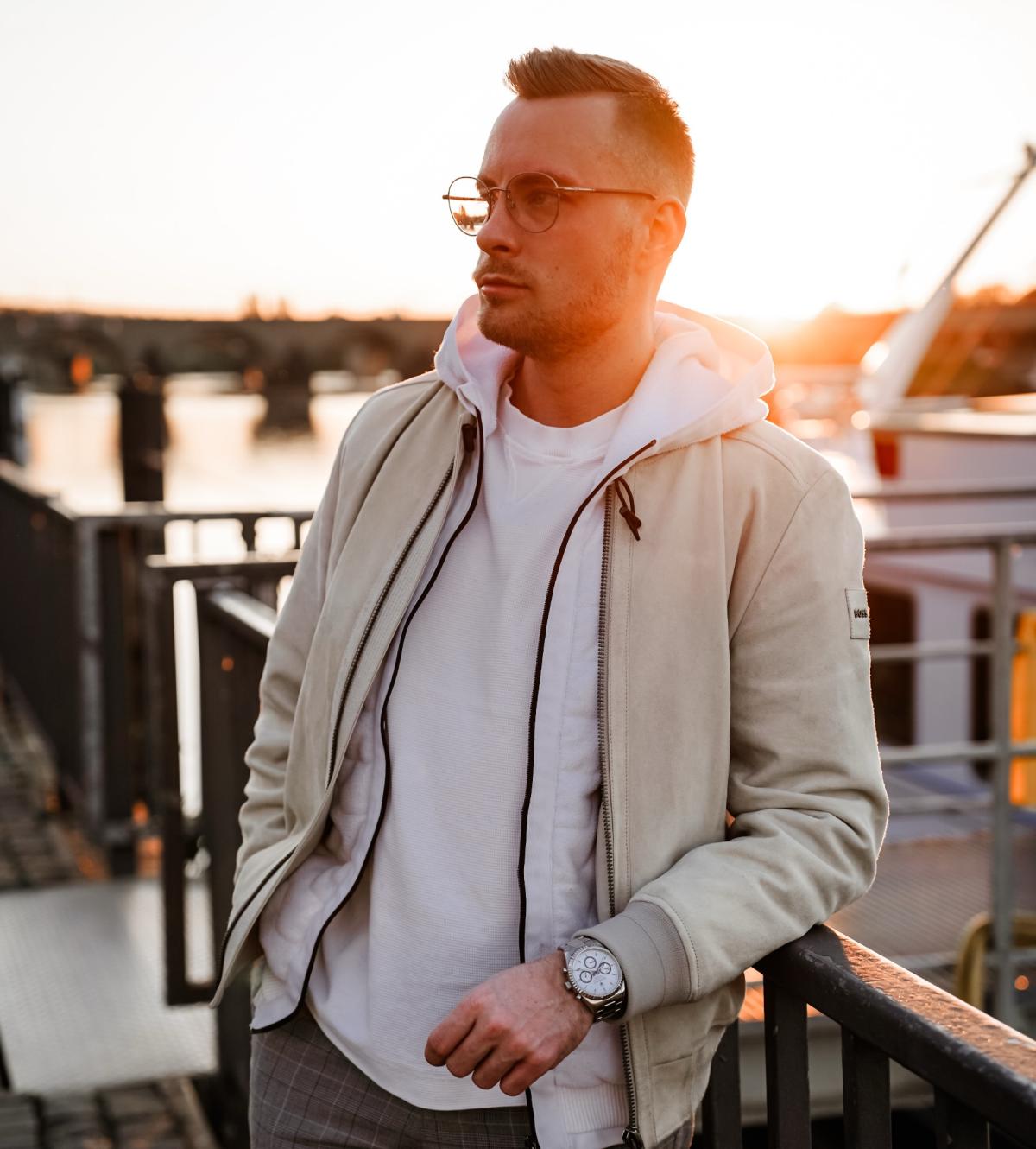 Mann mit Sonnenbrille und Jacke am Wasser bei Sonnenuntergang, Thema DJ Gage 2026.
