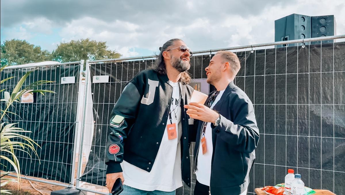Zwei DJs lachen und kommunizieren hinter der Bühne, sichtbar für DJ-Erfolg.