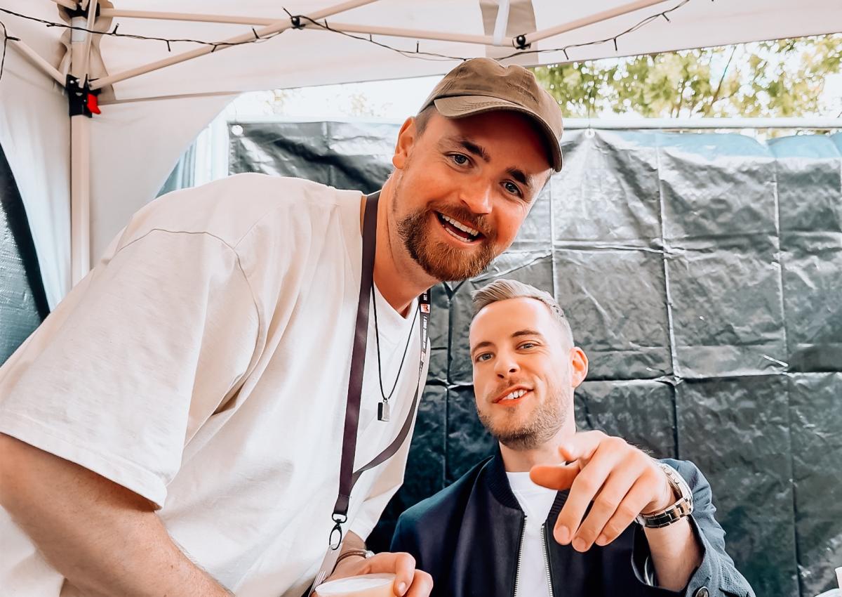 Zwei Männer unter einem Zelt, die entspannt über DJ-Erfolg sprechen.