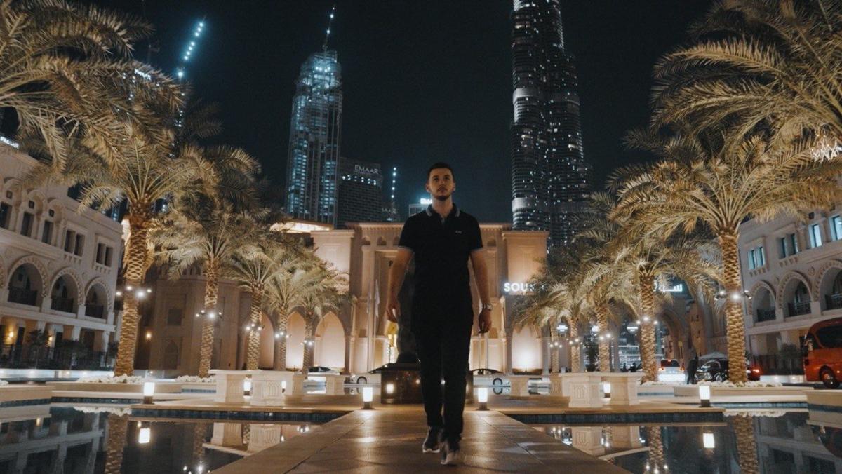 Mann geht nachts in Dubai entlang moderner Gebäude und Palmen für große Trading-Gewinne.
