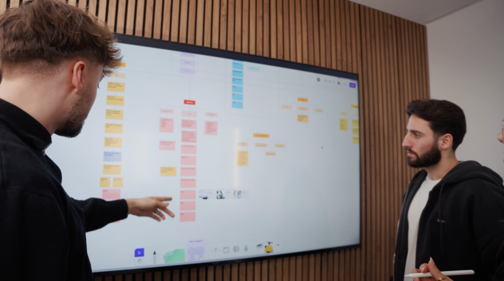 Teamdiskussion über Webflow, WordPress und Framer vor einem digitalen Board.