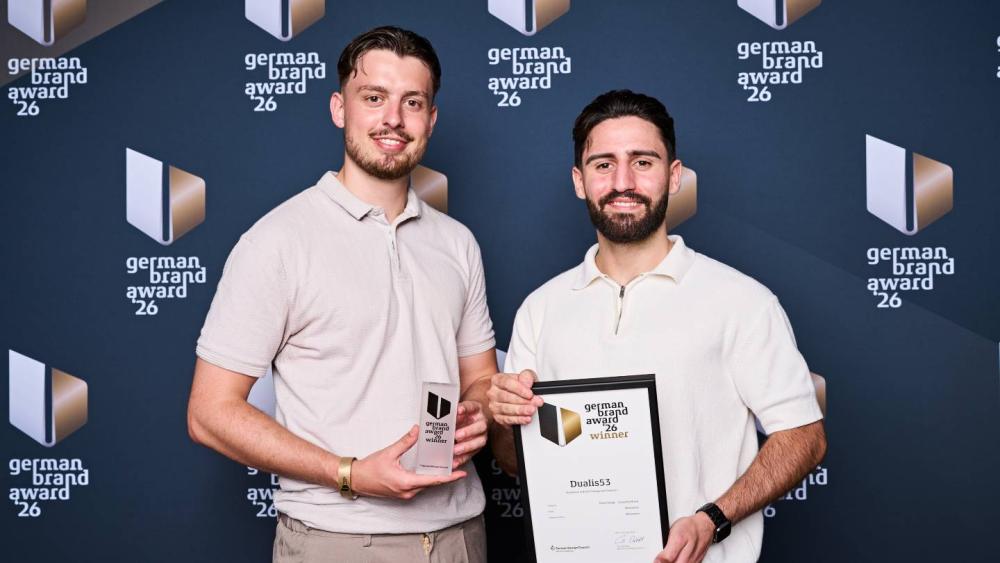 Zwei Preisträger halten den German Brand Award 2026 in der Hand.