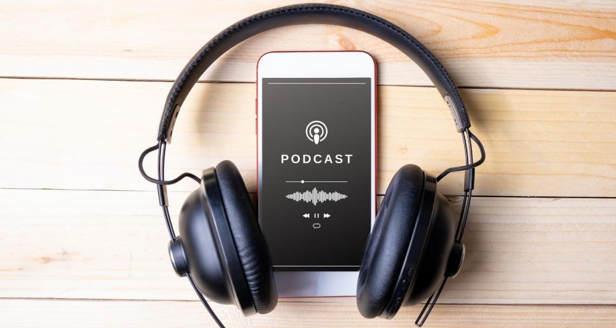Smartphone mit Podcast-Logo und Kopfhörern auf Holzoberfläche.