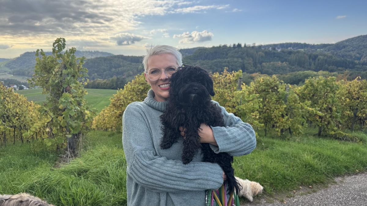 Eine Frau hält einen Bolonka Zwetna im Arm, umgeben von Weinbergen.