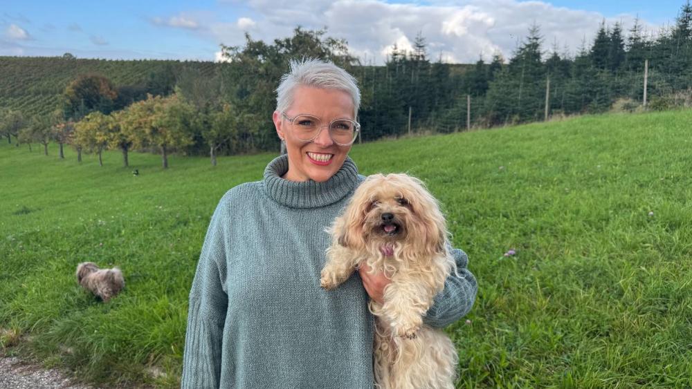 Eine Frau hält ihren Bolonka Zwetna im Feld und lächelt glücklich.